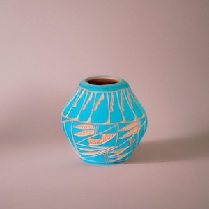 May include: A turquoise ceramic vase with a unique design. The vase features a series of tan-colored geometric patterns. The interior of the vase is a dark brown color. The vase is a decorative item.