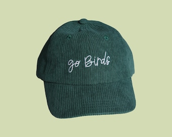 May include: A dark green corduroy baseball cap with the embroidered text "go Birds" in white script. The cap has a curved brim and a button on top. The hat is a classic style, suitable for casual wear.