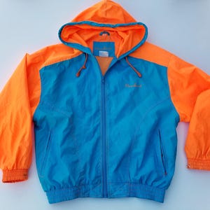 Könnte beinhalten: Eine leuchtend blaue und orangefarbene Kapuzenjacke mit durchgehendem Reißverschluss. Die Jacke hat einen blauen Körper mit orangefarbenen Ärmeln und Kapuze. Auf der Brust ist das Wort "Northland" gestickt.