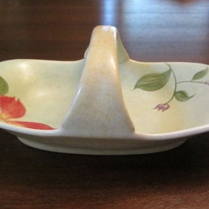 May include: A small, pale green ceramic serving dish with a handle. The dish is decorated with painted flowers in shades of red, green, and purple.