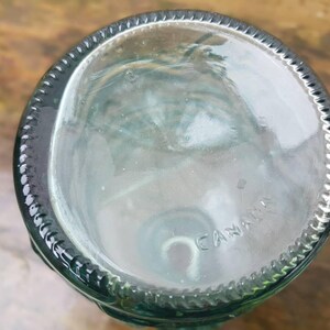 Peut inclure: Base d'une bouteille en verre clair, teint&eacute; de vert, avec un bord textur&eacute;. Le mot "CANADA" est estamp&eacute; au fond. La conception de la bouteille sugg&egrave;re qu'elle peut &ecirc;tre utilis&eacute;e pour des boissons ou &agrave; des fins d&eacute;coratives.