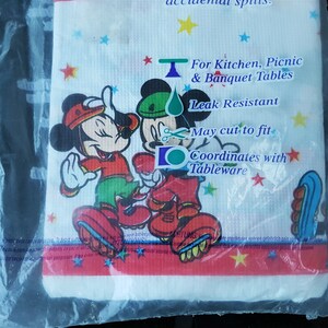 以下が含まれることがあります： ミッキーとミニーマウスが祝祭衣装を着た、白の耐漏れ性テーブルクロス。デザインにはカラフルな星と「キッチン、ピクニック、宴会テーブル用」というテキストが含まれています。テーブルクロスは透明なビニール袋に包装されています。
