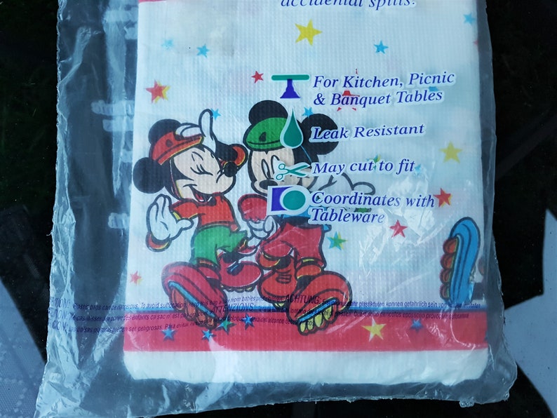 以下が含まれることがあります： ミッキーとミニーマウスが祝祭衣装を着た、白の耐漏れ性テーブルクロス。デザインにはカラフルな星と「キッチン、ピクニック、宴会テーブル用」というテキストが含まれています。テーブルクロスは透明なビニール袋に包装されています。