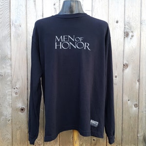 May include: Black long-sleeve shirt with the text "Men of Honor" printed on the back. The shirt has a small "Roots" logo on the bottom right corner.