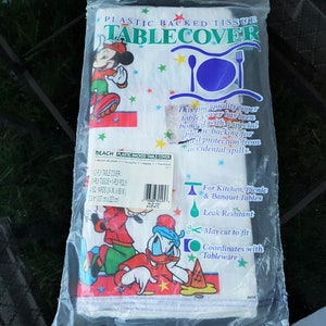 以下が含まれることがあります： 透明なプラスチックパッケージに入った、プラスチック裏打ちのティッシュテーブルクロス。テーブルクロスには、漫画のキャラクター、ミッキーマウスとドナルドダックが描かれています。パッケージには「Plastic Backed Tissue Tablecover」と書かれています。テーブルクロスの幅は137cmです。