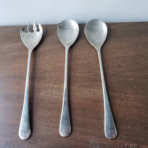 May include: Three silver serving utensils, a fork and two spoons, are arranged on a wooden surface.