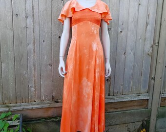 May include: A long, flowing orange dress with a white tie-dye pattern. The dress has a ruffled collar and short sleeves.