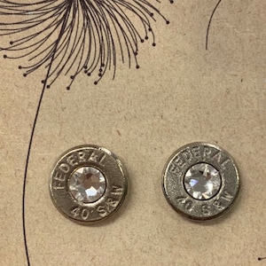 May include: A pair of silver bullet earrings with clear rhinestones. The bullets are engraved with "FEDERAL 40 S&W".