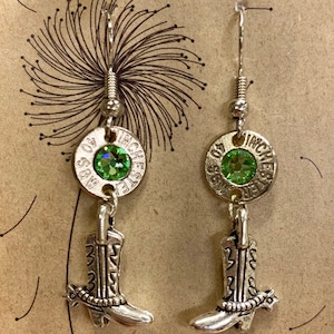 Op de afbeelding: Zilveren oorhangers met groene strass steentjes en een zilveren laars bedel. Het ronde deel van de oorhangers is gemarkeerd met "40 S&S 40 WINCHESTER INCHES".