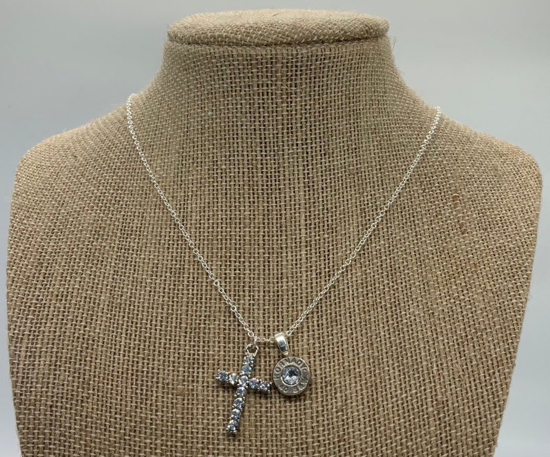 May include: A silver chain necklace with a rhinestone cross pendant and a silver bullet charm.