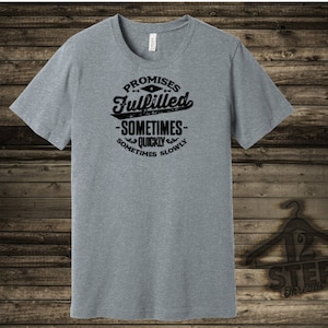 May include: Gray heather v-neck t-shirt with black text that reads "Promises Fulfilled - Sometimes Quickly Sometimes Slowly".