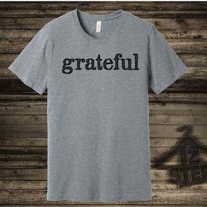 Puede incluir: Una camiseta gris jaspeada con la palabra "agradecido" impresa en negro en la parte delantera.