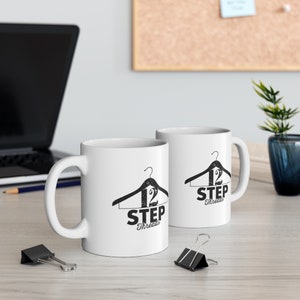 May include: Two white ceramic mugs with black text and a hanger graphic. The text on the mugs reads "12 Step Threads".
