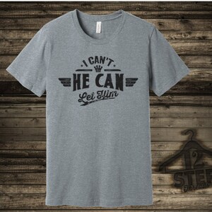 May include: A heather grey t-shirt with a black graphic that reads "I Can't He Can Let Him" with a crown and wings.