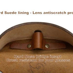 K&ouml;nnte beinhalten: Ein braunes Leder-Brillenetui mit einem Futter aus Wildleder. Das Etui hat einen harten Nasensteg-Einsatz, um Brillen vor dem Zerkratzen zu sch&uuml;tzen. Der Text "Standard Suede lining - Lens antiscratch protection" und "Hard Nose bridge insert Crush resistant for your glasses" ist auf dem Etui aufgedruckt.