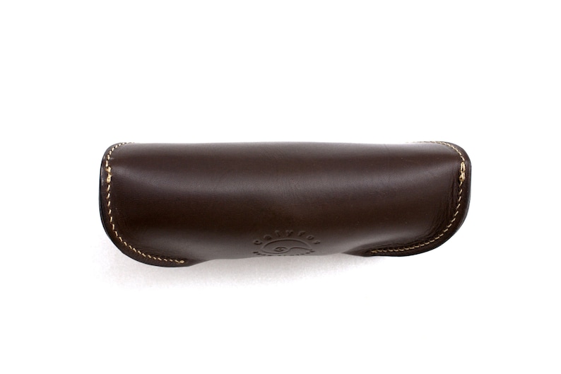 May include: A dark brown leather sunglasses case with a curved design. The case has a stitched border with gold thread and a debossed logo on the front. The case is designed to protect eyewear.