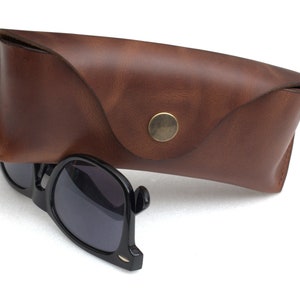 May include: A brown leather case with a brass button closure, and a pair of black sunglasses with dark lenses.