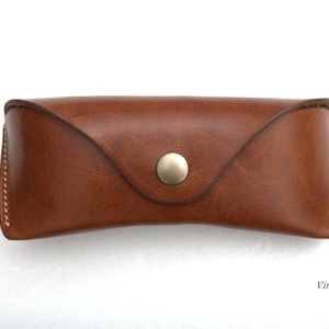 K&ouml;nnte beinhalten: Ein braunes Lederetui f&uuml;r Brillen mit einem Druckknopfverschluss. Das Etui hat eine Vintage-braune Farbe.