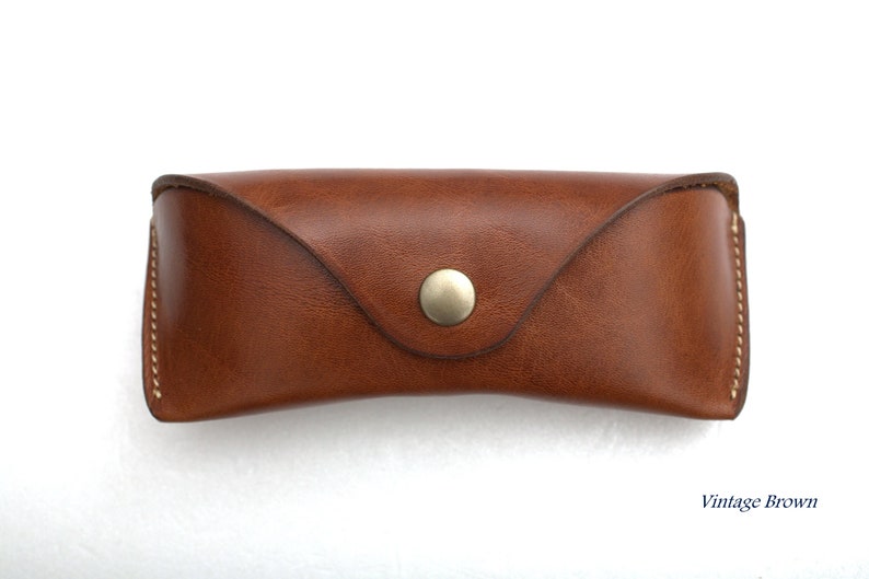 K&ouml;nnte beinhalten: Ein braunes Lederetui f&uuml;r Brillen mit einem Druckknopfverschluss. Das Etui hat eine Vintage-braune Farbe.