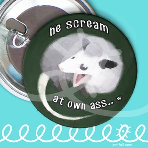 May include: A round pin-back button featuring a dark green background and a white illustration of an opossum with its mouth open. The text "he scream at own ass.. w" is printed in white letters with a black outline around the central opossum graphic.