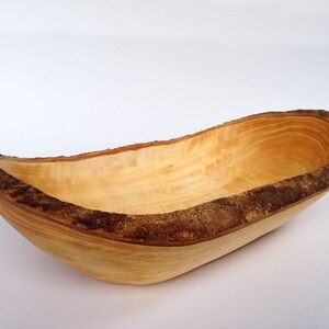 May include: A large, oval-shaped wooden bowl with a natural wood finish. The bowl has a thick, uneven rim that is made from the bark of the tree. The bowl is perfect for serving salads, fruit, or other snacks.