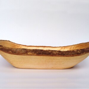 May include: A wooden bowl with a natural bark edge. The bowl is light brown and has a smooth, polished finish.