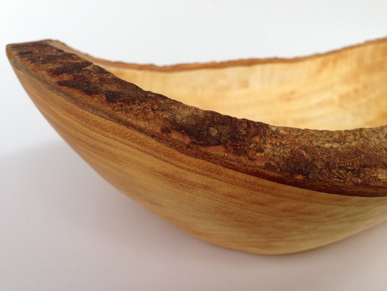 May include: A wooden bowl with a natural bark edge. The bowl is light brown and has a smooth, rounded interior.