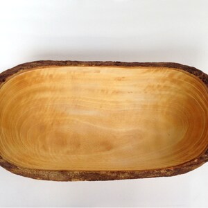May include: A wooden bowl with a natural bark edge. The bowl is oval shaped and has a smooth, light brown interior.