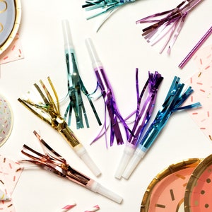 Puede incluir: Un conjunto de artículos para fiestas con temática de donut. El conjunto incluye platos de papel, servilletas, sombreros de fiesta, silbatos y pajitas. Los platos y las servilletas tienen un patrón de chispas rosas y blancas, mientras que los sombreros de fiesta tienen un patrón de chispas rosas y blancas con un borde dorado. Los silbatos son coloridos y tienen serpentinas adjuntas. Las pajitas son de rayas rosas y blancas.