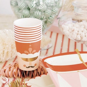 Puede incluir: Un plato de papel rojo y blanco en forma de tambor con ribetes dorados y un diseño rosa y blanco. El plato está sobre un mantel a rayas rojas y blancas con tenedores dorados.