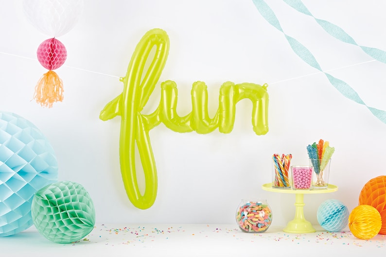 May include: A green inflatable balloon spelling out the word "fun" hanging from a white string. The balloon is surrounded by colorful honeycomb balls and candy.