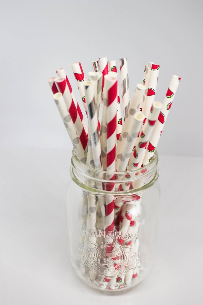 May include: A glass jar filled with red and white striped paper straws with watermelon print. The jar has the text "Bernardin" on the side.
