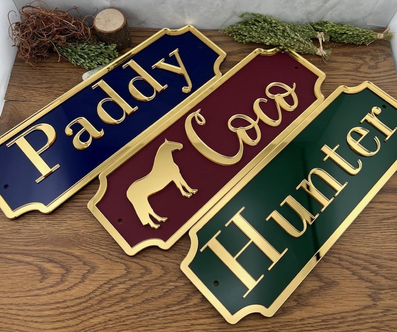 May include: Three rectangular nameplates in navy blue, burgundy, and hunter green with gold lettering. The navy plate reads "Paddy", the burgundy plate reads "Coco" with a horse silhouette, and the green plate reads "Hunter".