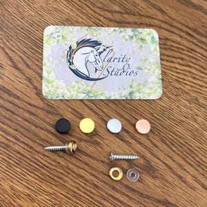 May include: A selection of small hardware items, including screws, washers, and decorative caps in black, gold, silver, and copper. A business card with a horse logo and the text "Clarity Studios" is also present.