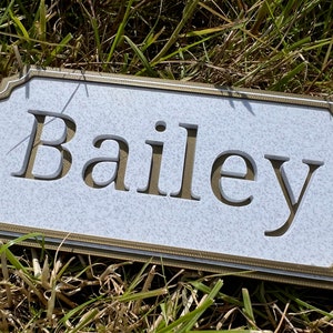 May include: A white plaque with a gold border and the name "Bailey" engraved in gold lettering.