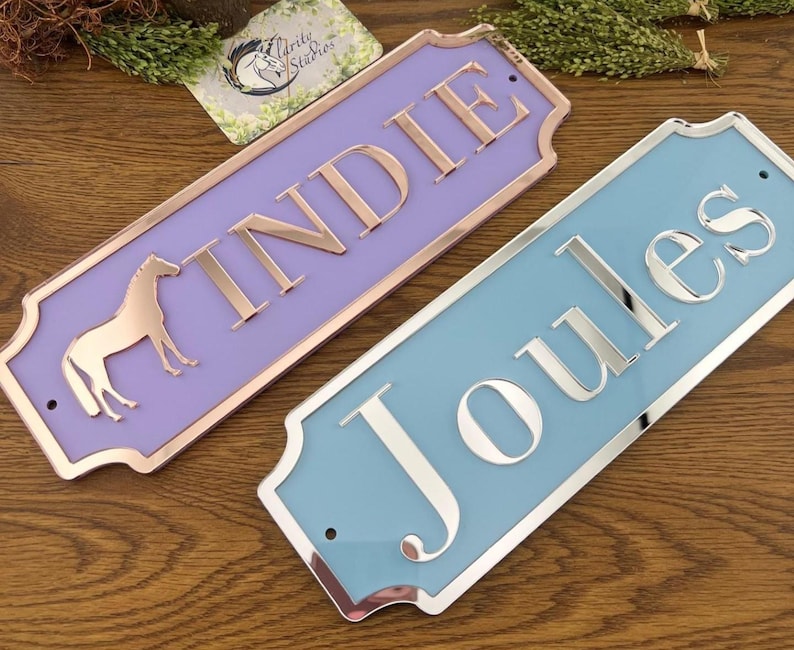 May include: Two rectangular nameplates. One is lavender with rose gold trim and lettering, and a horse silhouette. The other is light blue with silver trim and lettering. Both have rounded corners.