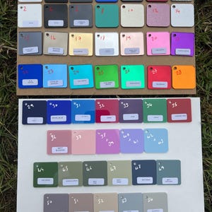 May include: A collection of 54 square color swatches arranged on two white boards. The swatches display a variety of colors, including blue, green, pink, and gray. Each swatch is labeled with a number and color name.