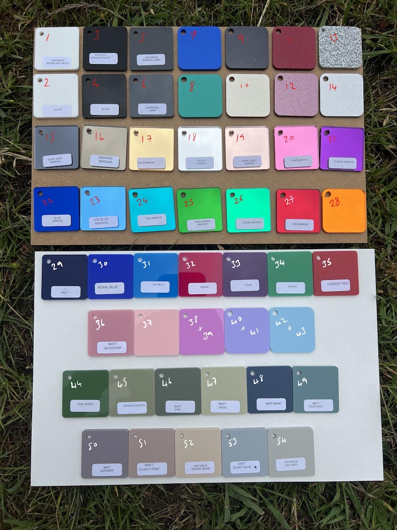 May include: A collection of 54 square color swatches arranged on two white boards. The swatches display a variety of colors, including blue, green, pink, and gray. Each swatch is labeled with a number and color name.