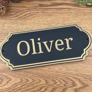 May include: A black and gold personalised nameplate with the name "Oliver" in gold lettering.