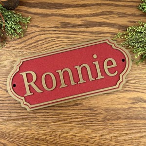 May include: A red and gold personalised nameplate with the name "Ronnie" in gold lettering.