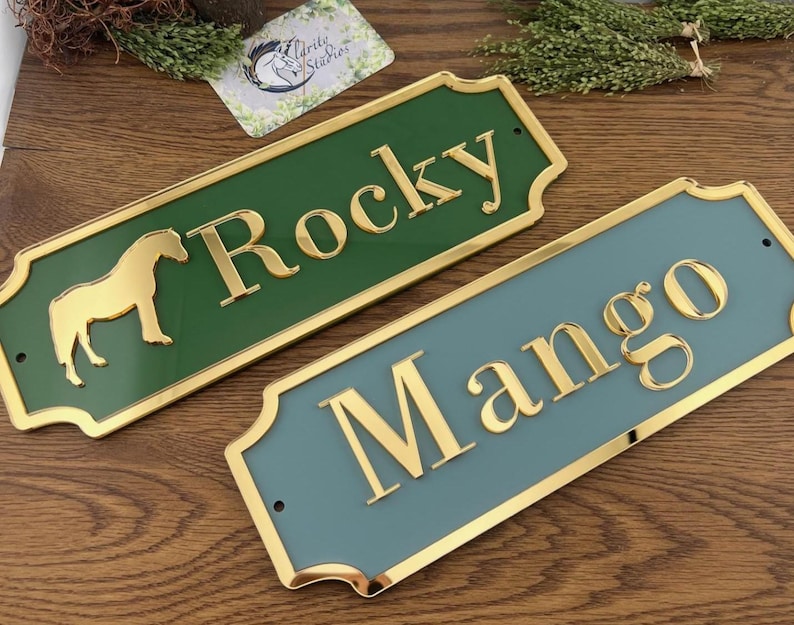 May include: Two rectangular horse nameplates. One is green with "Rocky" in gold lettering and a gold horse silhouette. The other is blue-green with "Mango" in gold lettering. Both have gold trim.