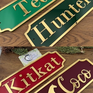 May include: Rectangular name signs in green, dark green, red, and burgundy with gold lettering. The names "Ted", "Hunter", "Kitkat", and "Coco" are displayed. The "Coco" sign features a gold horse silhouette.