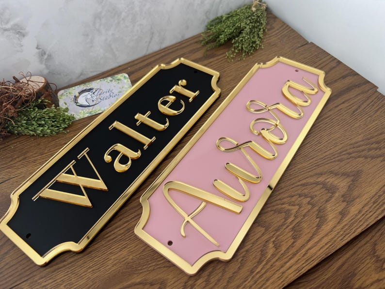 May include: Two decorative nameplates, one black and one pink, with gold lettering and trim. The black plate reads "Walter", and the pink plate reads "Aurora". Both plates have a decorative shape.