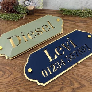 May include: Two rectangular plaques with scalloped edges and gold-coloured hardware. One plaque is sage green with the name Diesel cut out in gold. The other is navy blue with the name Levi and the numbers 01234 567891 cut out in gold.