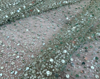 May include: A close-up of a light green fabric with sequins and small pearls. The fabric has a shimmery, iridescent look.