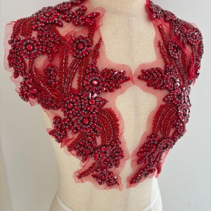 May include: Red beaded applique with floral designs on a sheer mesh fabric. This applique is perfect for adding a touch of sparkle and elegance to any garment.