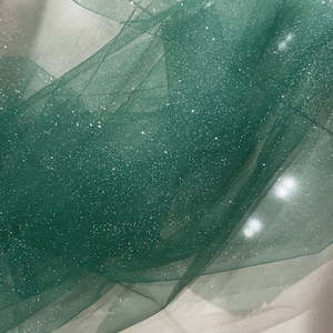 May include: Green sparkly tulle fabric with a fine mesh texture. The fabric is soft and delicate, with a subtle shimmer.