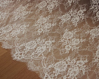 May include: White lace fabric with a delicate floral pattern. The lace has a scalloped edge.
