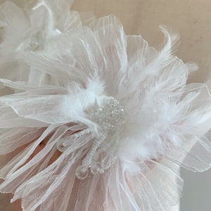 May include: A white flower embellishment with delicate tulle petals and feathers, accented with crystal beads.