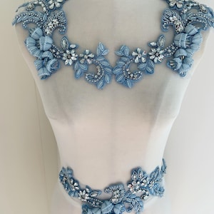 May include: A light blue floral applique set, featuring intricate beadwork and sparkling crystal accents. The set includes shoulder and waist embellishments, perfect for adding a touch of elegance to garments. The design incorporates floral and leaf patterns.